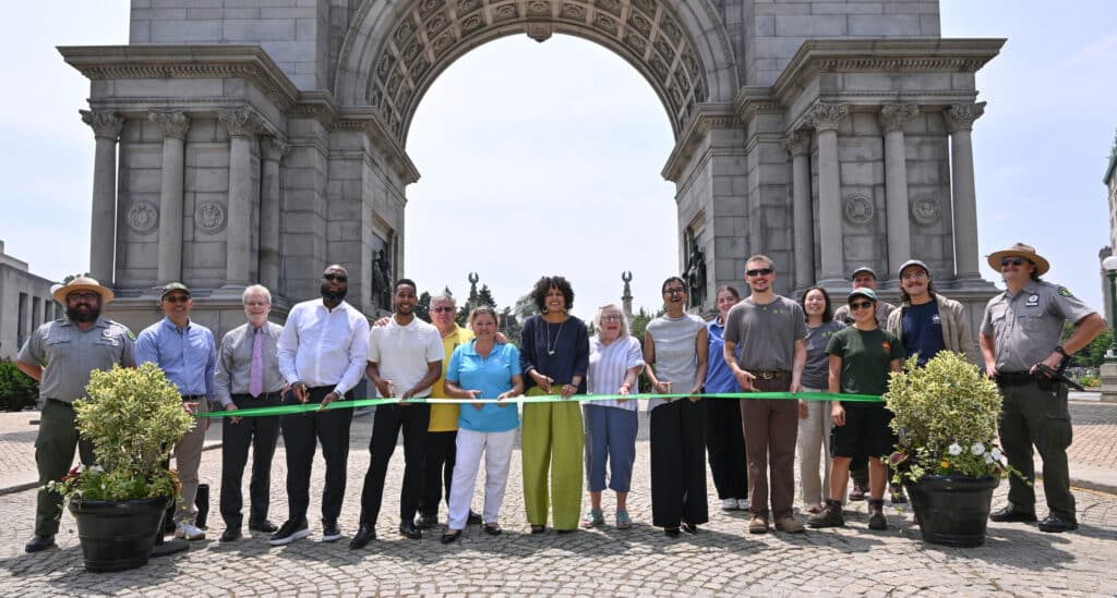 Group cuts green ribbon in front of the arch, celebrating the restoration of Grand Army Plaza.
